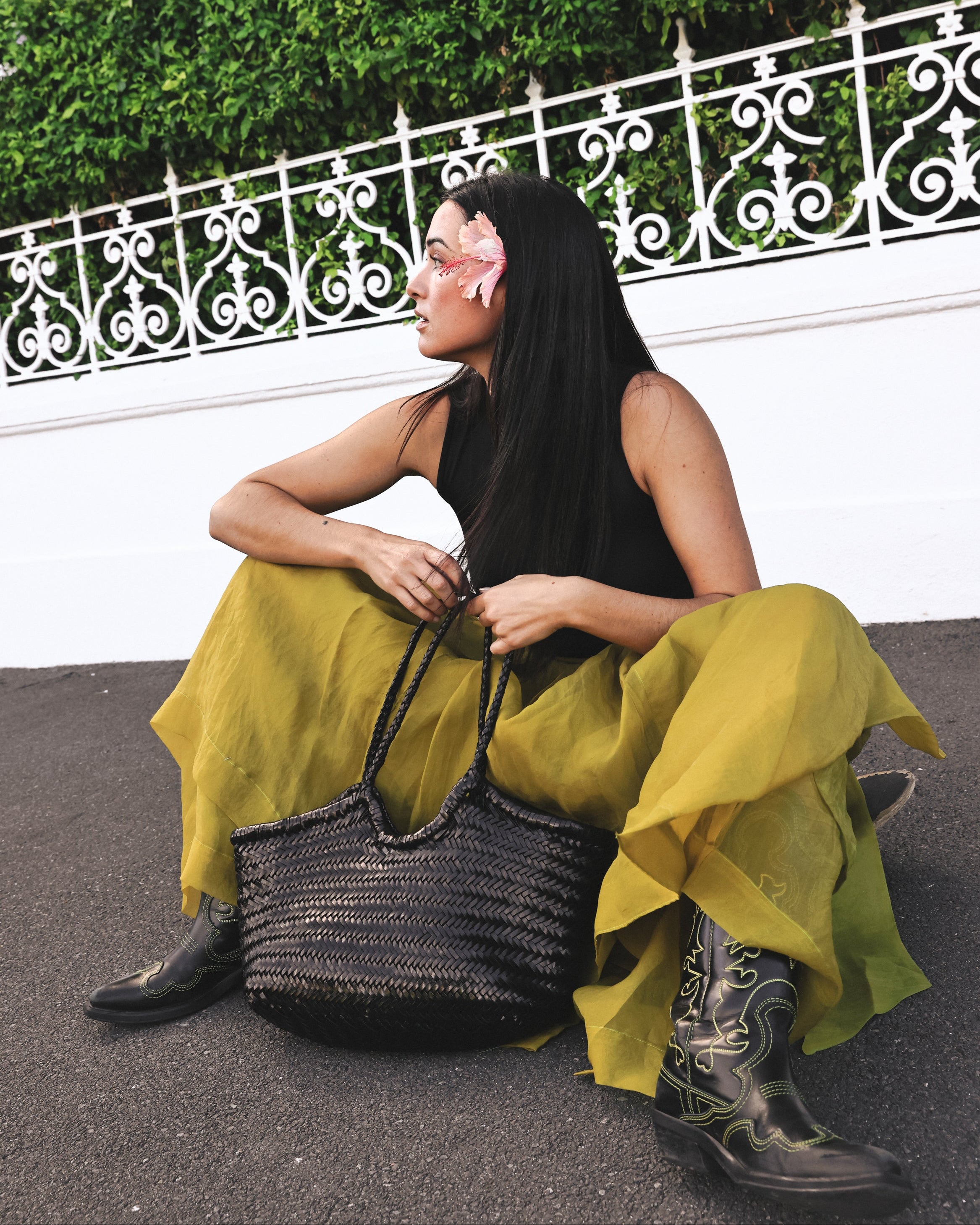 Woman sitting on a bench with a green skirt and black top, holding a woven bag.