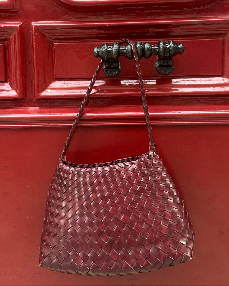 Woven handbag hanging on a red door with intricate black metalwork